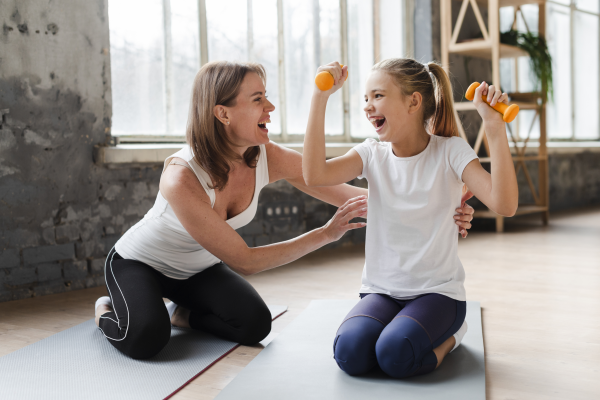 mother-tickling-daughter-holding-weights-yoga-mat